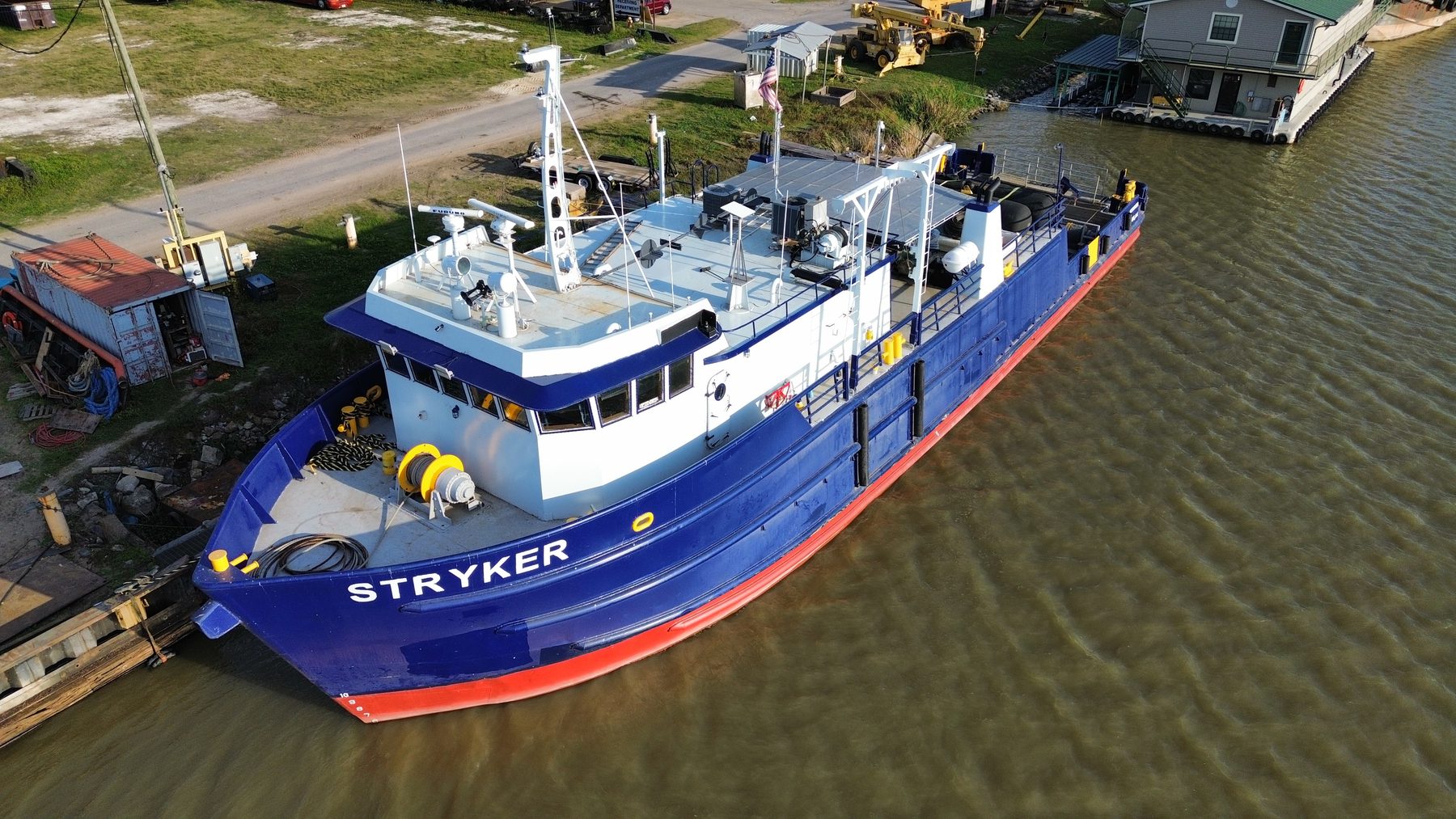 Aerial view of the M/V Stryker moored alongside a timber wharf, blue hull with red boot-topping